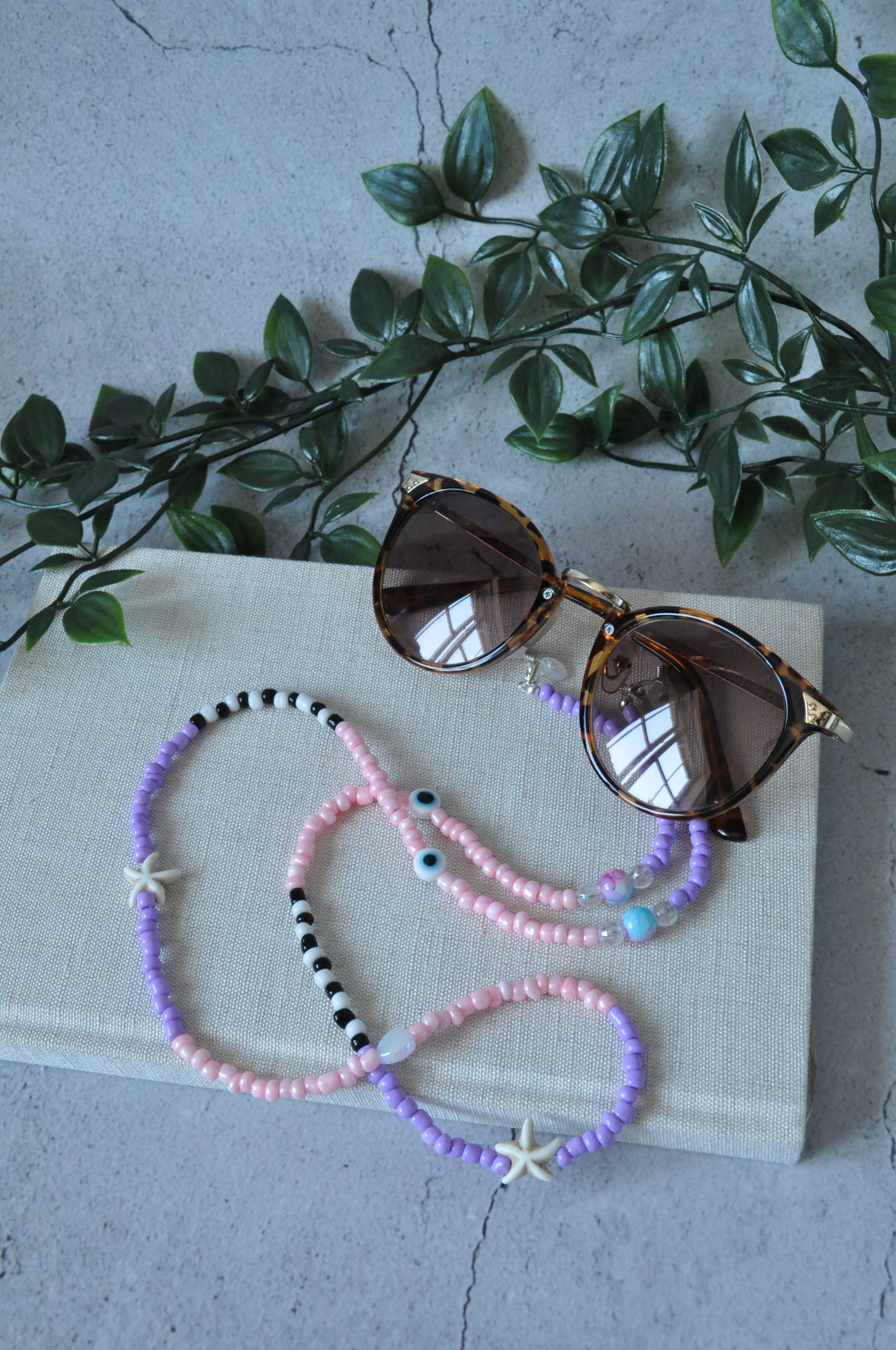 Lilac glass seed beads starfish glasses chain draped over a textured notebook on a grey background.