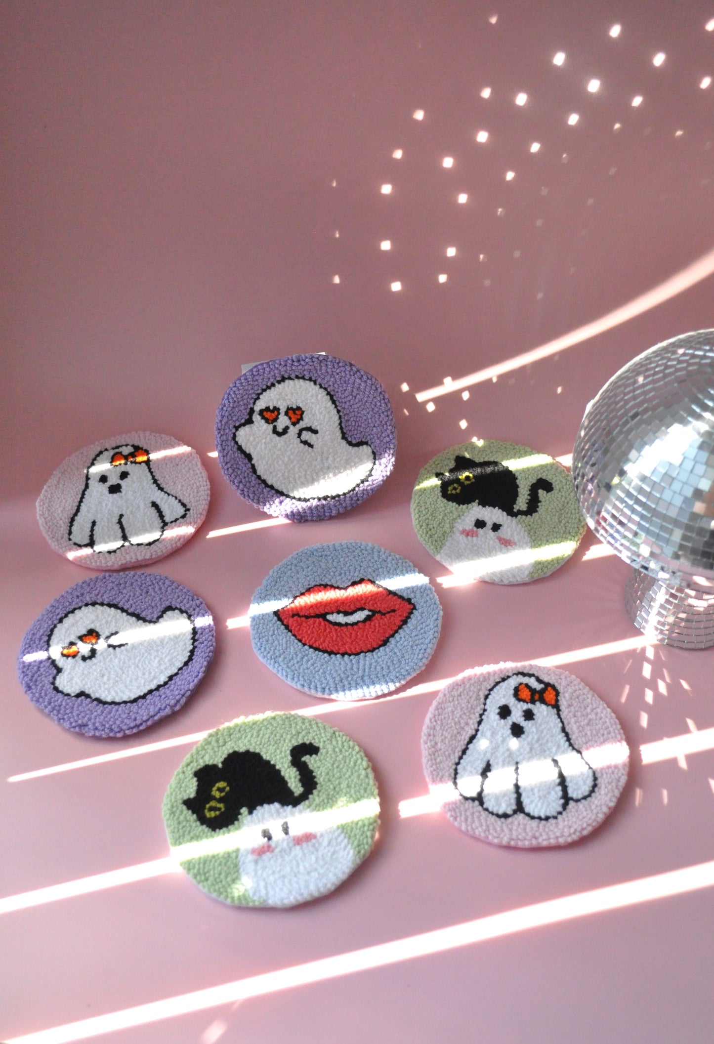 A set of Halloween-inspired mug rugs on a pink background. Designs include a flying cute ghost, playful lips, a spooky ghost with a cute bow, and a ghost with a cat. The rugs feature pastel colors like soft purples, pinks, and blues.