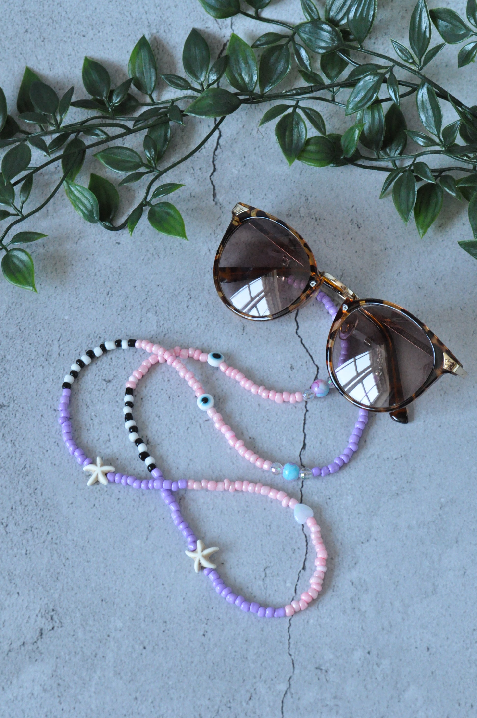 Lilac glass seed beads starfish glasses chain displayed with brown glasses on a grey background.