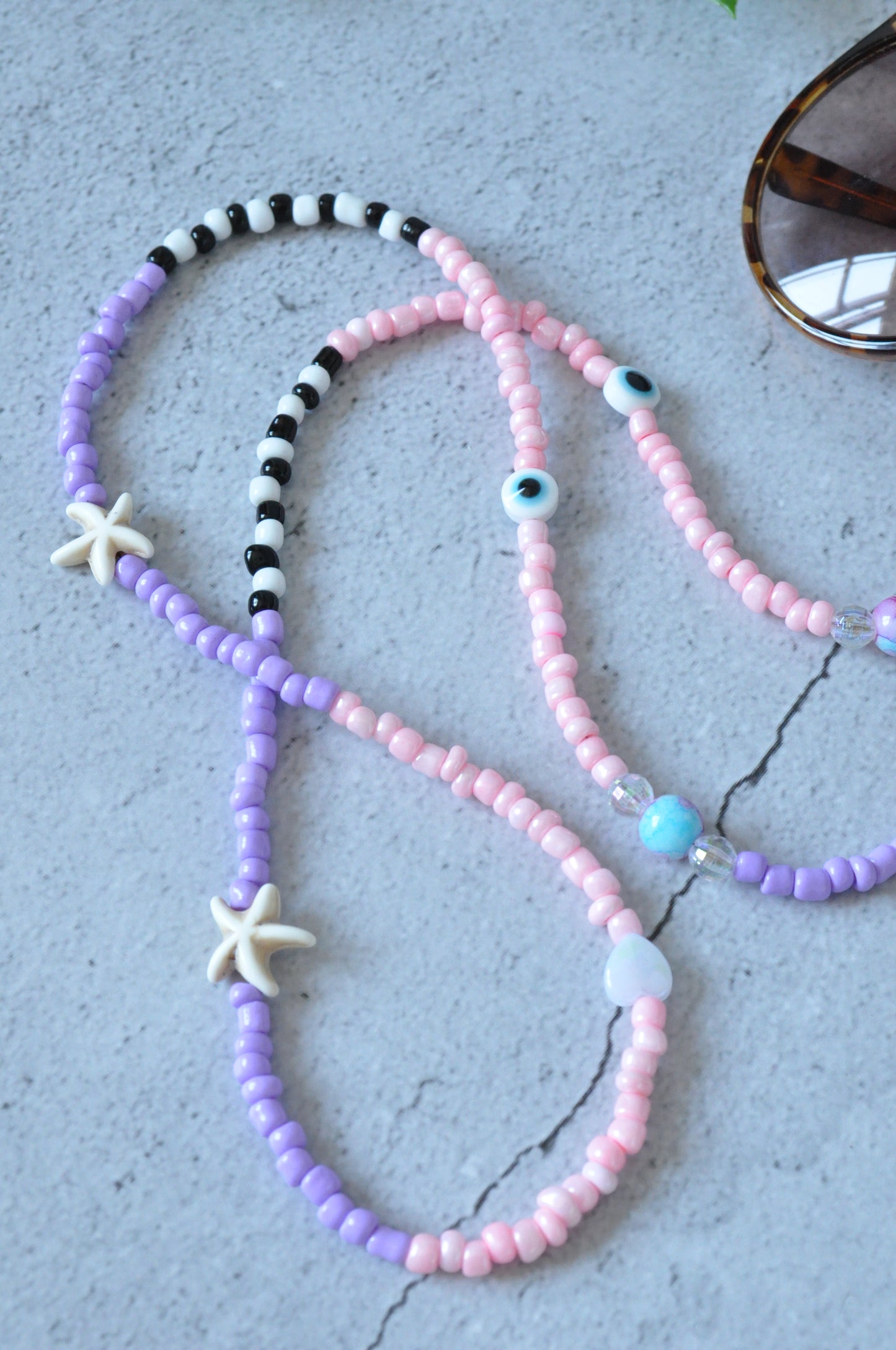 Close-up of the lilac glass seed beads on the starfish glasses chain, showcasing intricate details against a grey background.