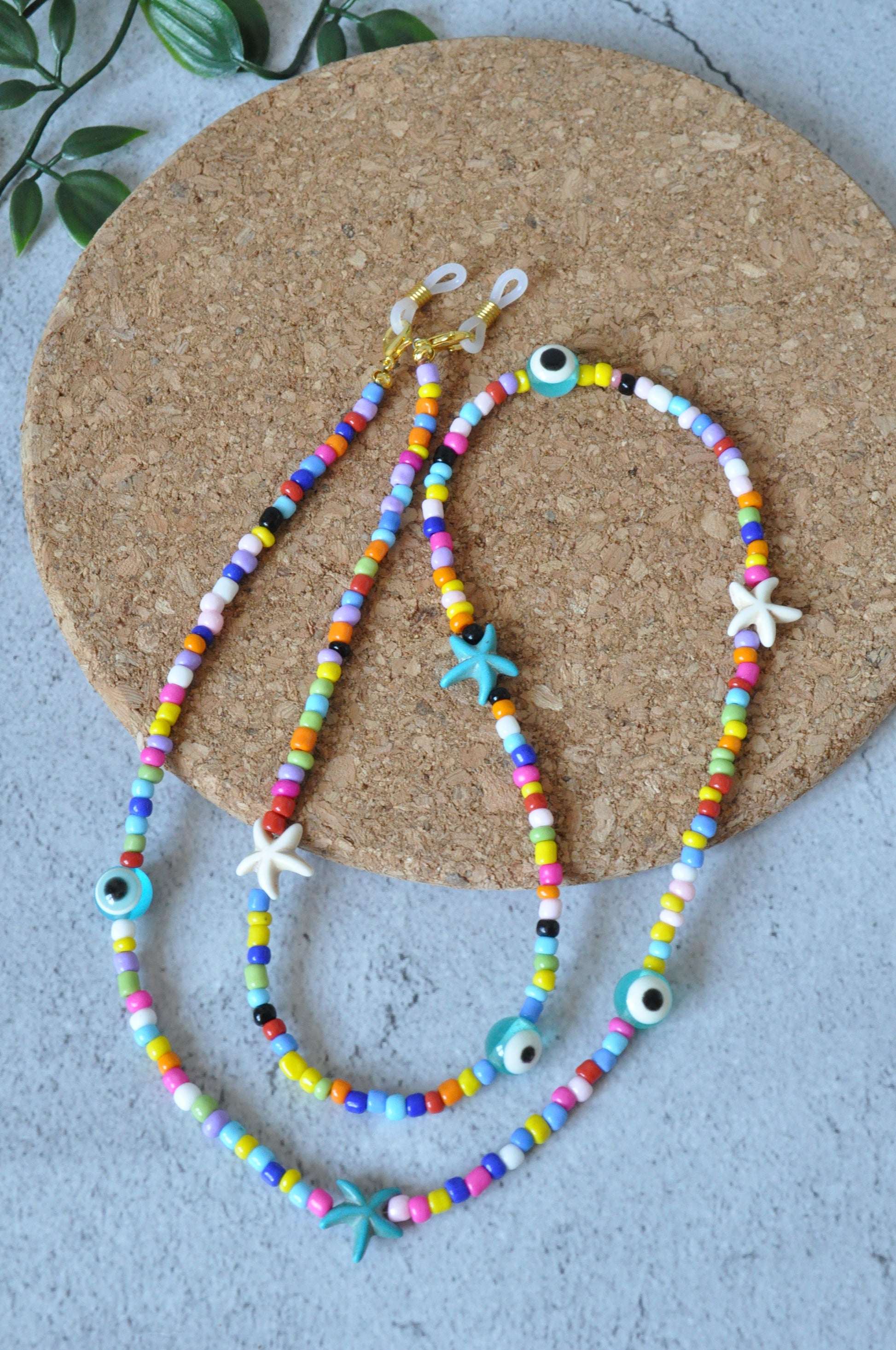 Colourful evil eye beaded glasses chain displayed on a cork surface against a grey background.