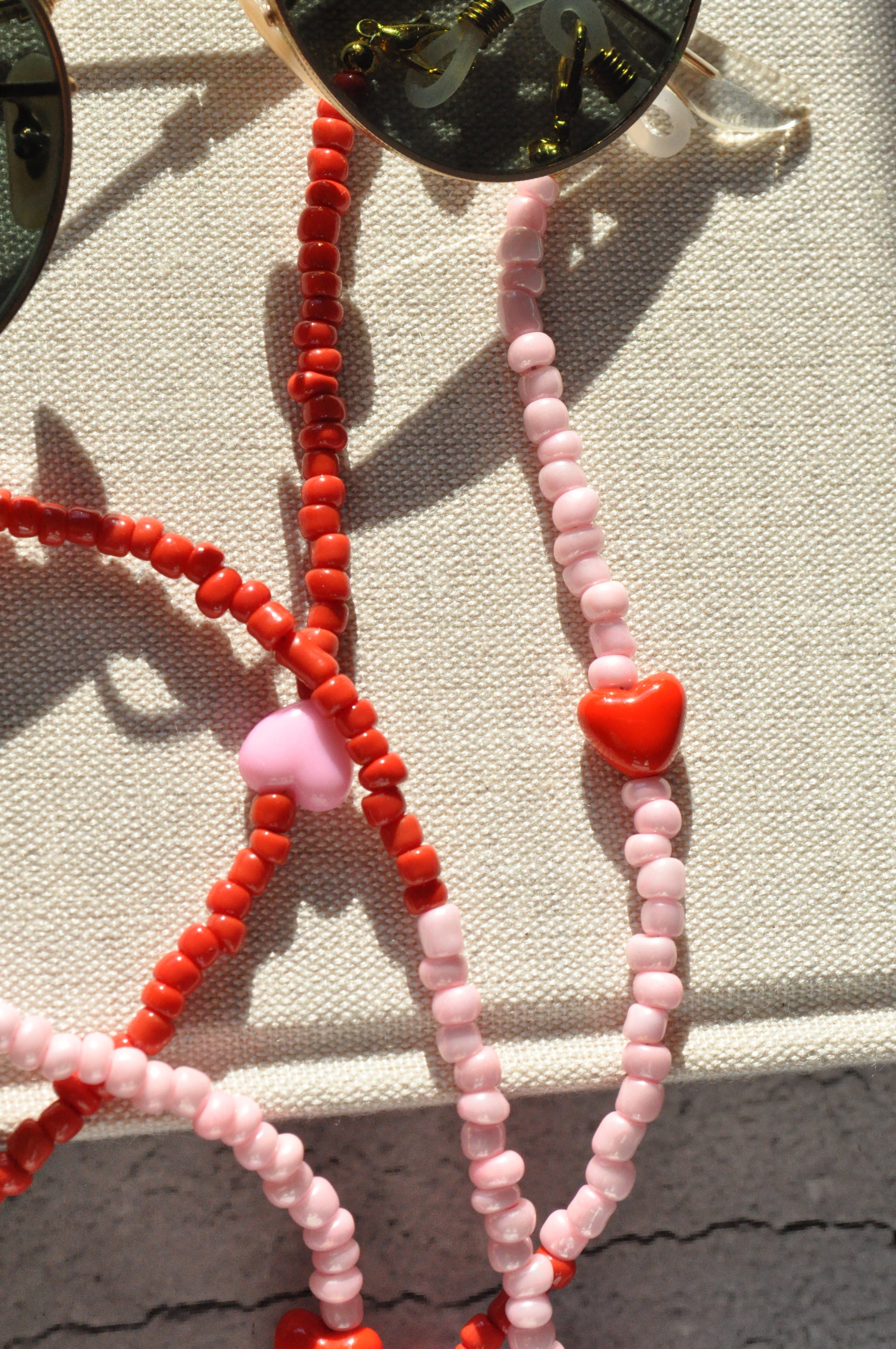 Close-up of the pink and red hearts glasses chain, showcasing the detailed beads on a textured surface with a grey background.