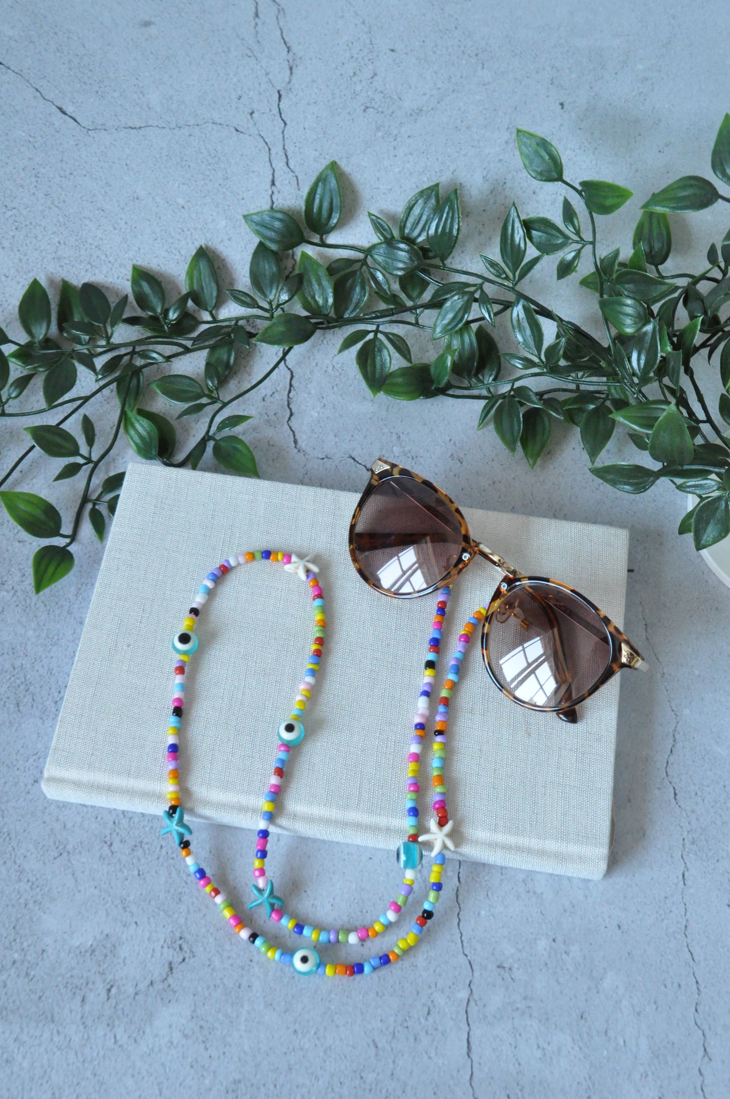 Colourful evil eye beaded glasses chain displayed on a cork surface against a grey background.