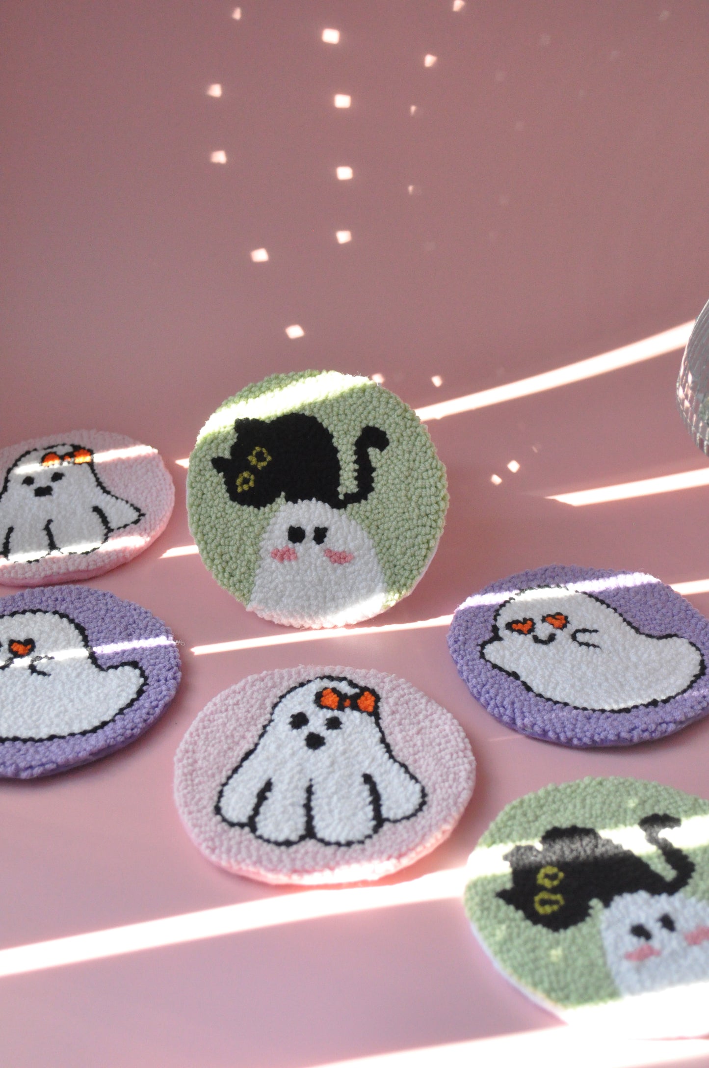 A set of Halloween-inspired mug rugs on a pink background. Designs include a flying cute ghost, playful lips, a spooky ghost with a cute bow, and a ghost with a cat. The rugs feature pastel colors like soft purples, pinks, and blues.