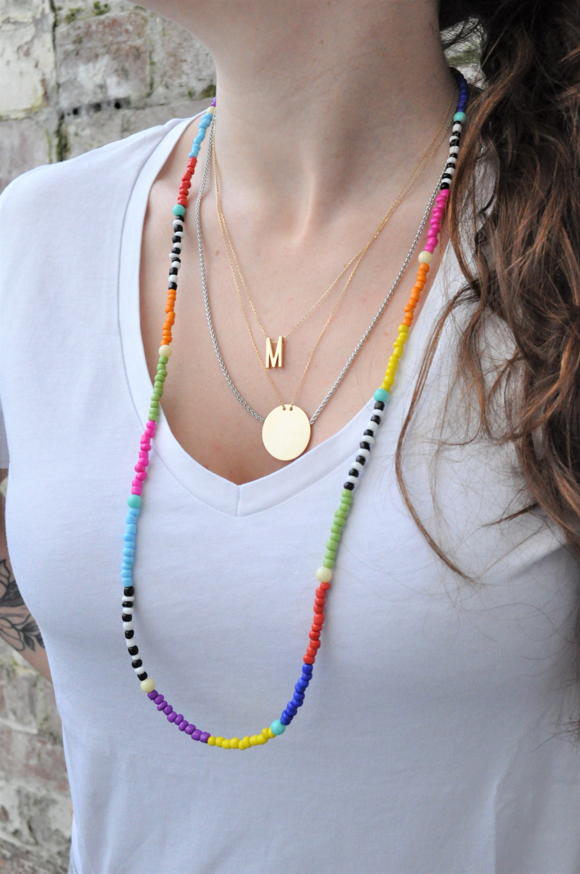 A long-haired girl wearing a white tee showcases the beaded glasses chain as a necklace. She pairs it with layered necklaces, highlighting the vibrant rainbow colours of the beads.