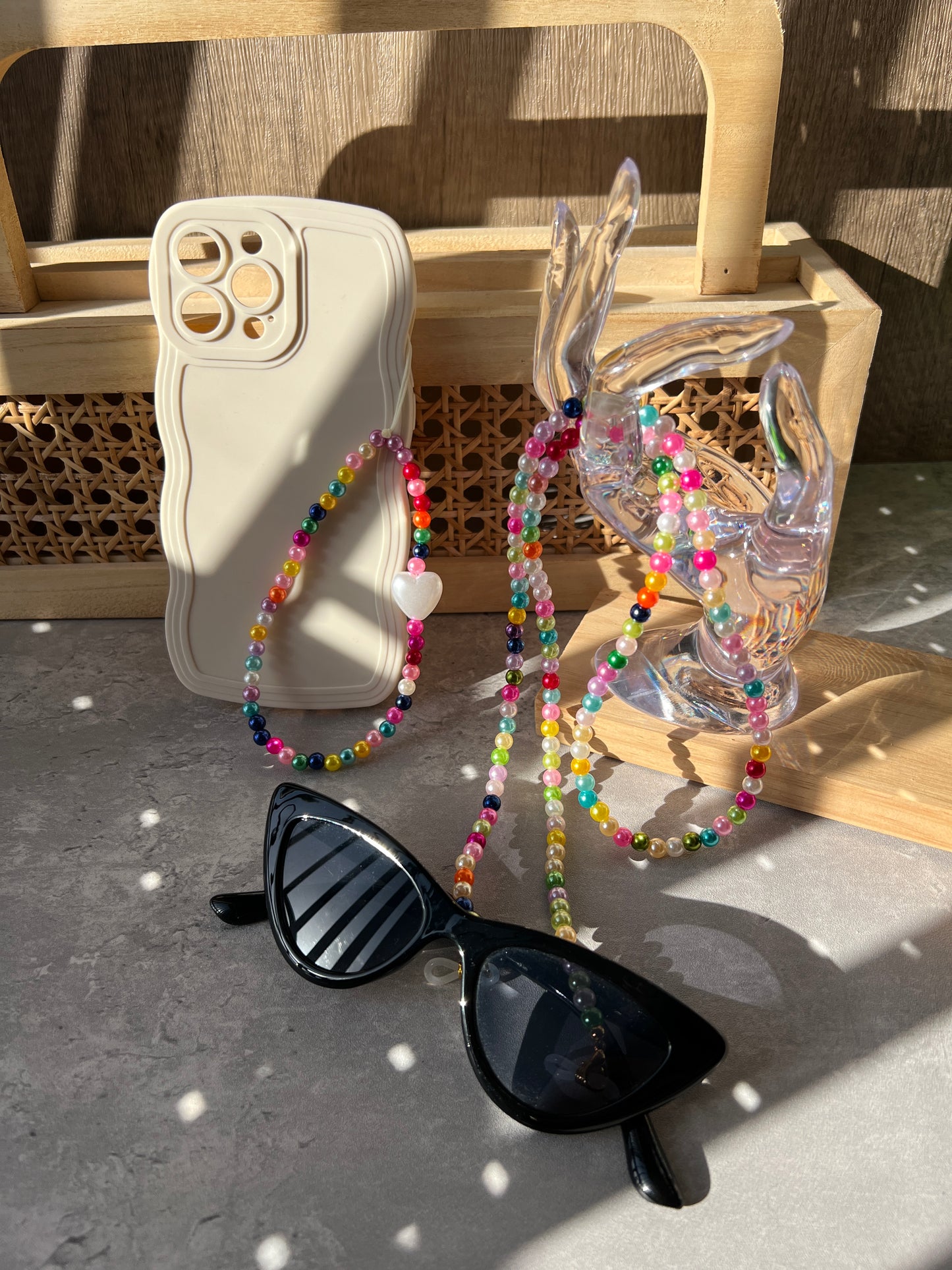 Rainbow Colourful Beaded Glasses Chain displayed on an acrylic transparent jewellery display hand, with a matching phone strap visible in the foreground, against a grey background.