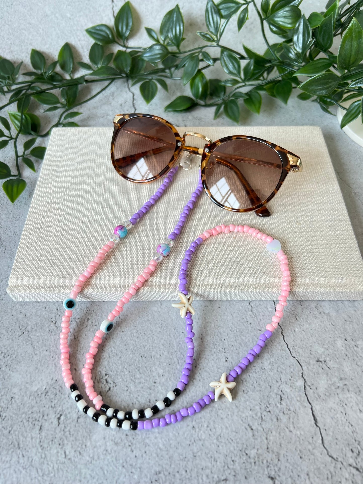 Lilac glass seed beads starfish glasses chain draped over a textured notebook on a grey background.