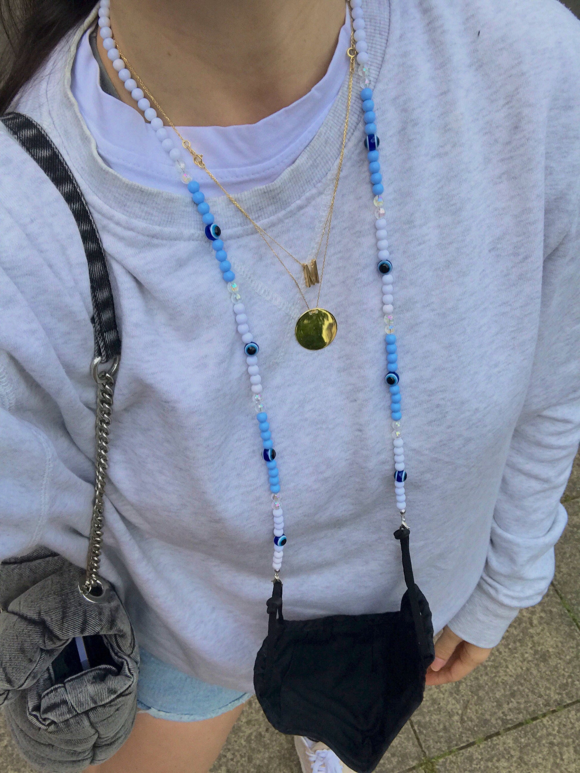  A girl wearing a grey sweatshirt models the blue Evil Eye Beaded Glasses Chain as a mask necklace. The chain, featuring high-quality beads and the iconic Evil Eye symbol, adds a stylish touch while keeping the mask securely in place.