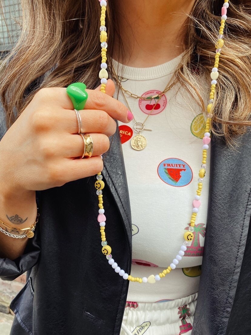 A girl in a colourful outfit models the smiley beaded glasses chain. The chain, featuring yellow seed beads and smiley faces, adds a playful touch to her vibrant attire.